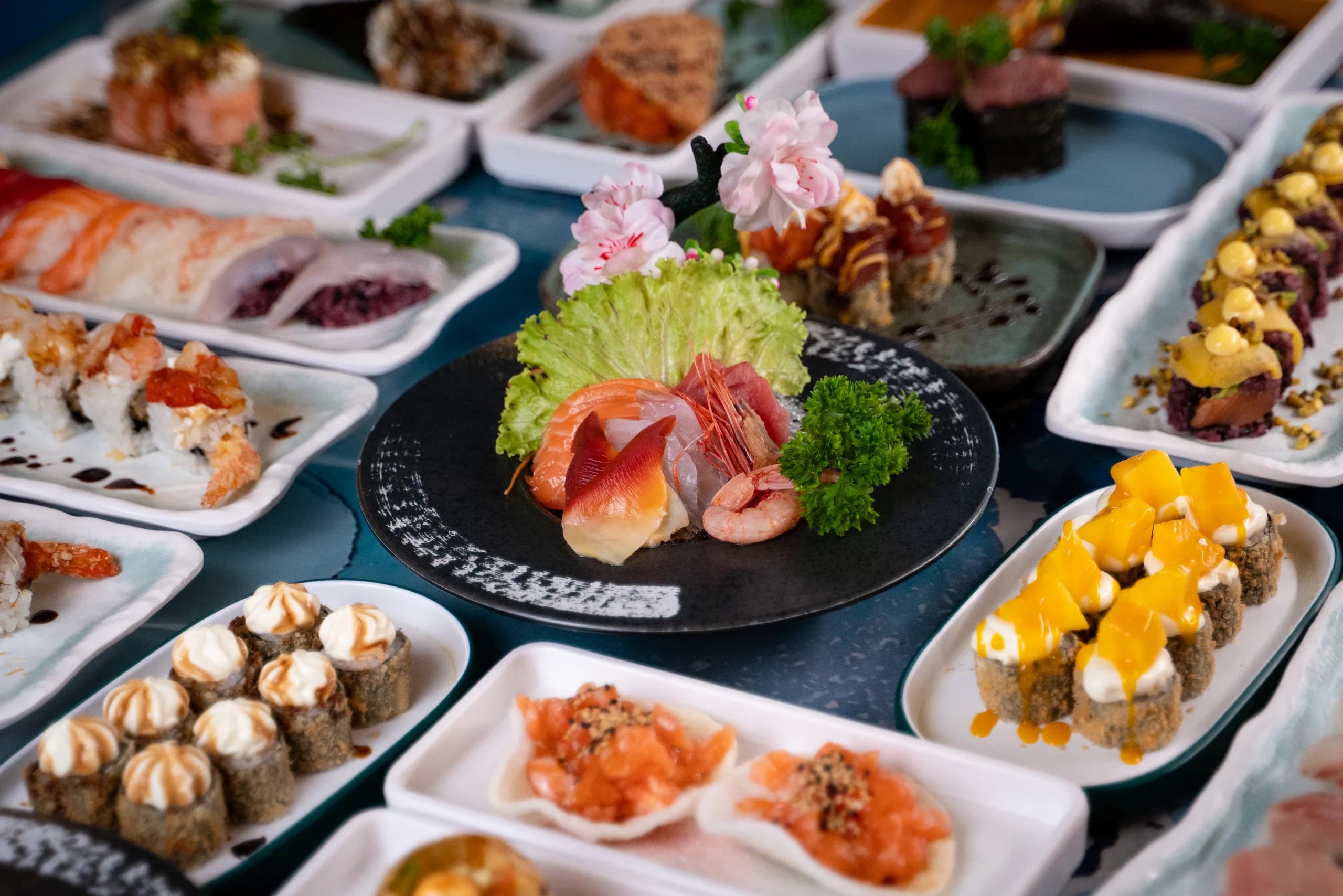 Tavola imbandita con sashimi al centro, roll e tartare di salmone tutto intorno