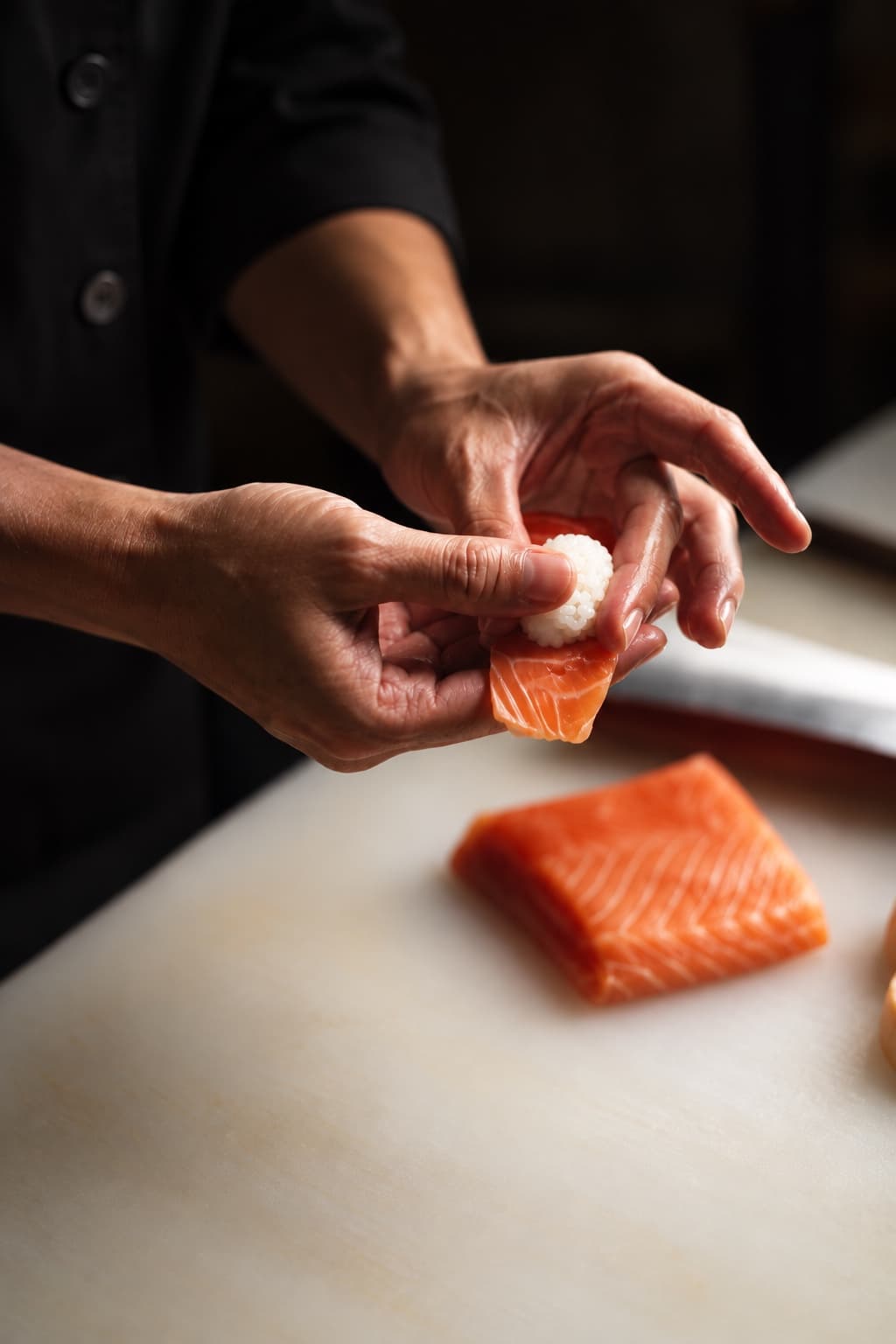 Mani che compongono un nigiri di salmone al banco